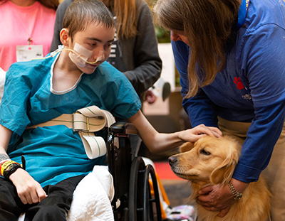 Devin LePes, a 19-year-old patient, pets Millie, a golden retriever, with handler Kay Schmidt.