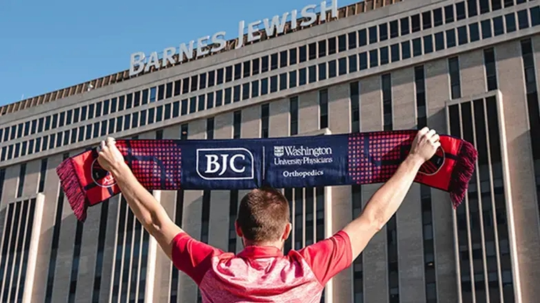 Man holding a BJC scarf over his head while standing in front of Barnes Jewish Hospital