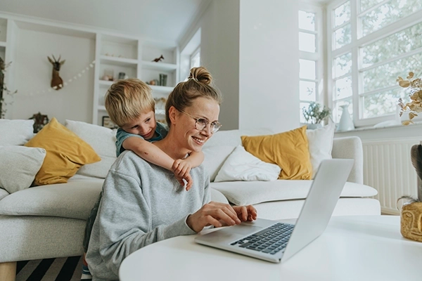 Woman using a laptop while a child hugs her