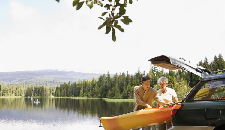 Two people unloading a kayak from the rear of a station wagon with a lake in the background. 