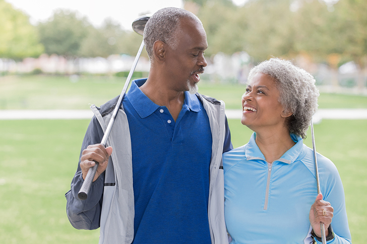 Couple holding golf clubs and smiling at eachother