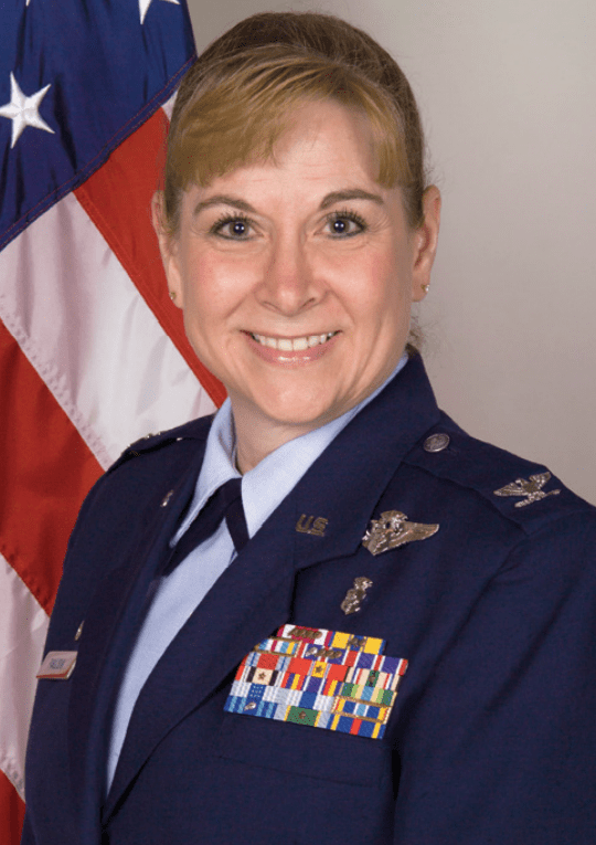Pennie Pavlisin pictured in an Air Force uniform with flag behind her.