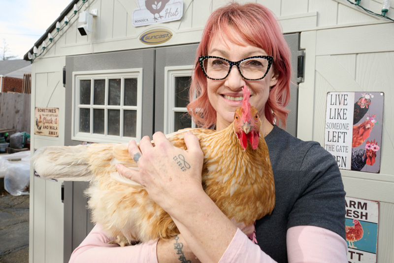 Debbi smiling and holding a chicken outside her backyard coop after endoscopic spine surgery.