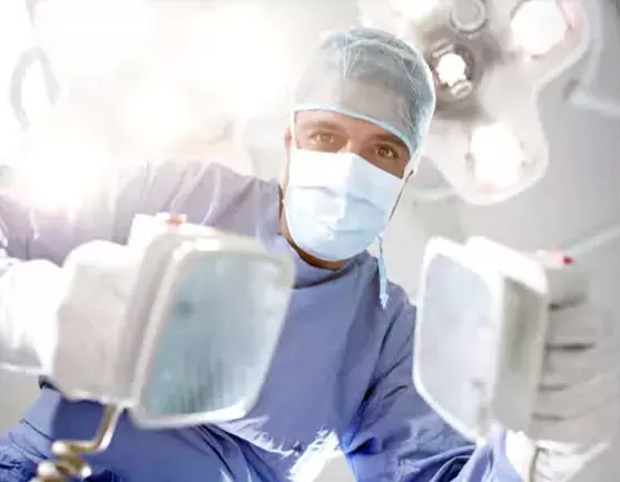 Doctor in full medical setup in an operating room holding defibrillator paddles.