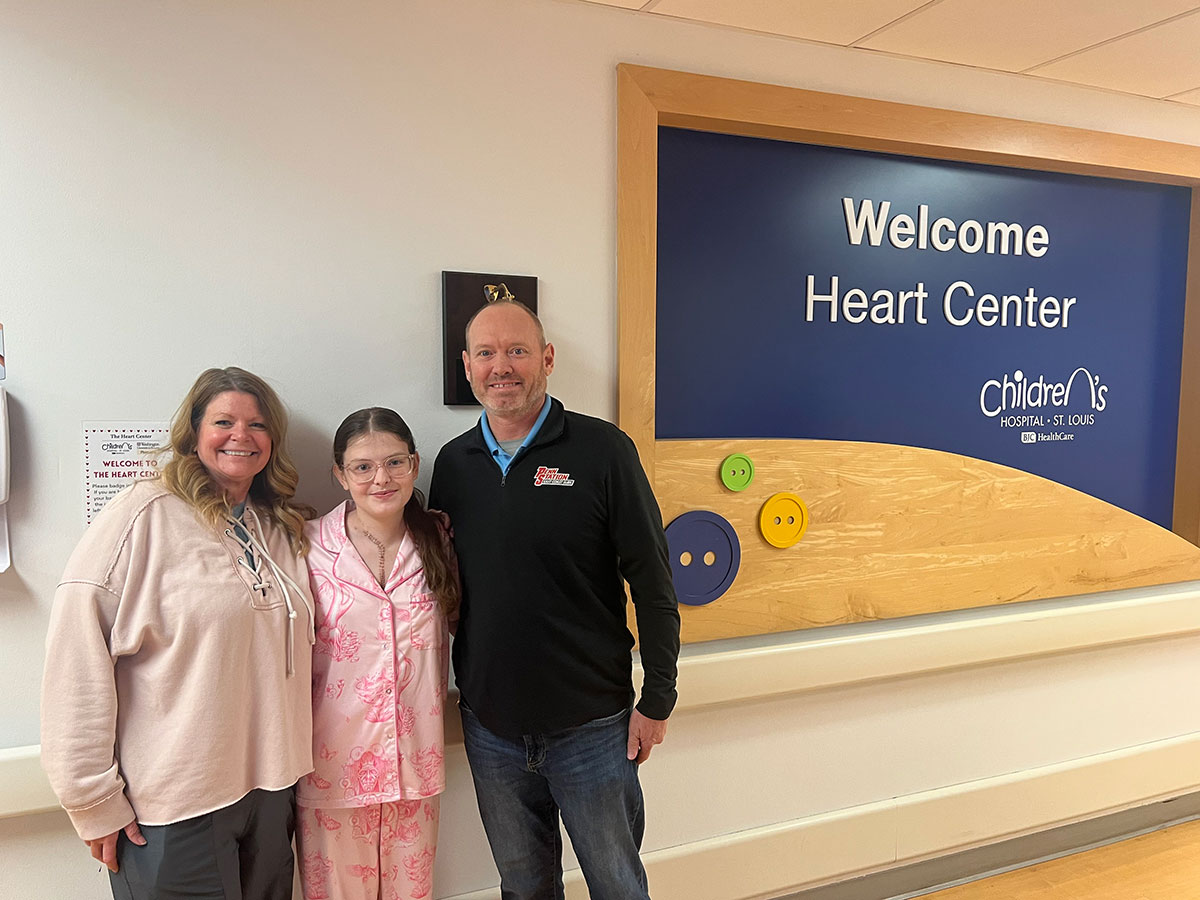 Macey and her parents standing in front of the "Welcome Heart Center" sign at St. Louis Children's Hospital
