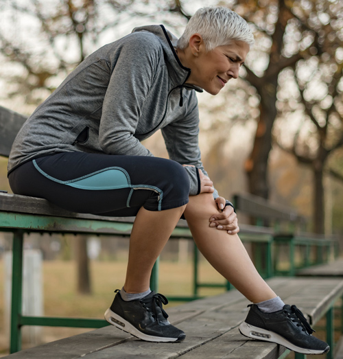 Woman sitting outside on a bench touching his knee