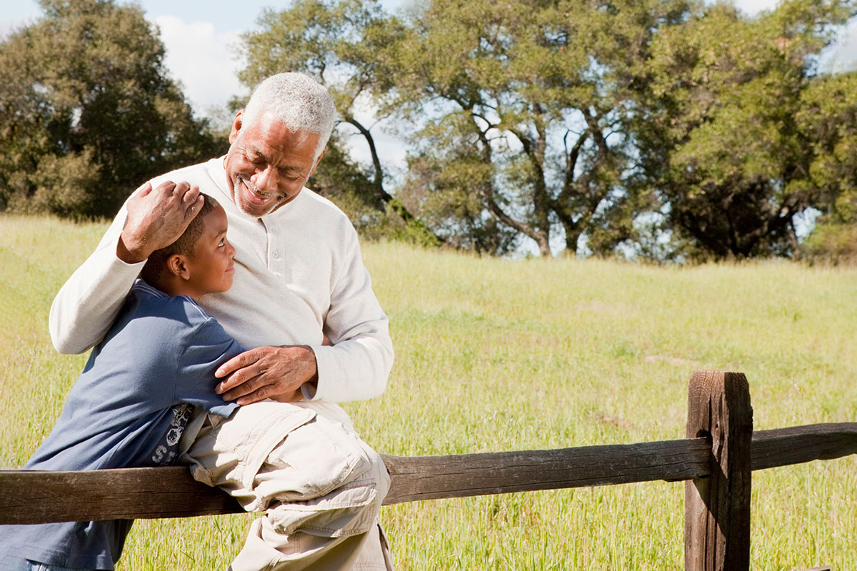 Senior man sitting on a fence outdoors with a younger child