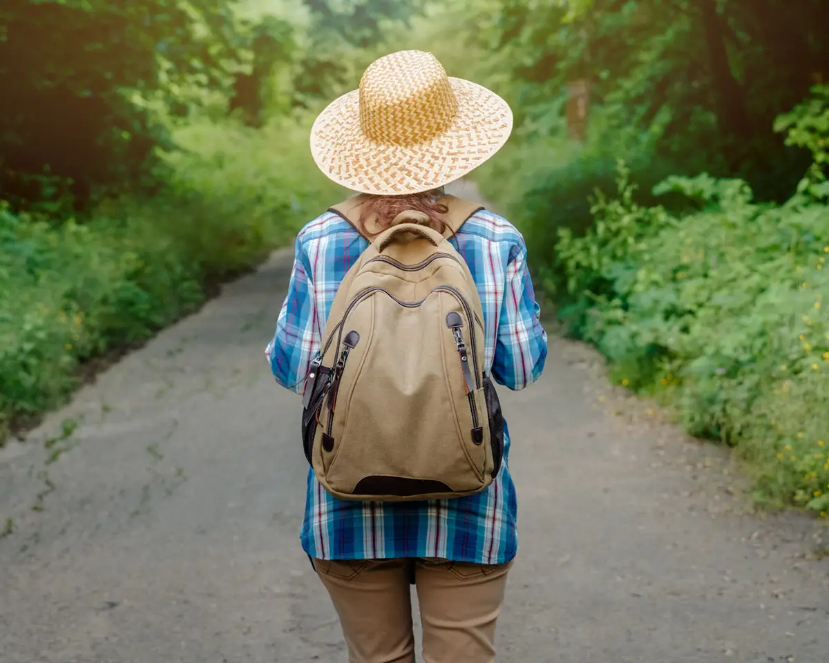 Woman walking outdoors in nature wearing a hat and backpack