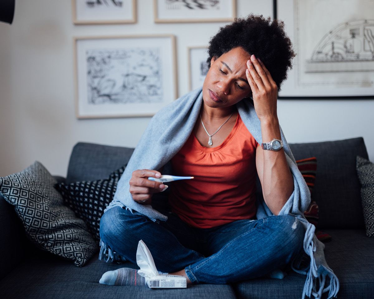 Woman sitting on couch looking at a thermometer
