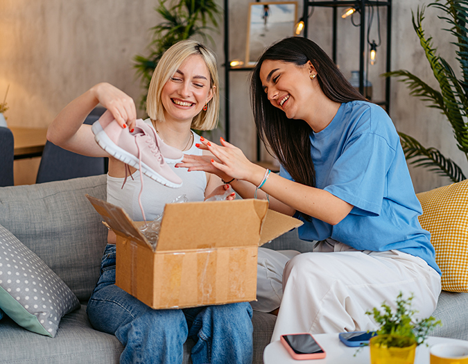 Two women opening a package that contains a pair of shoes