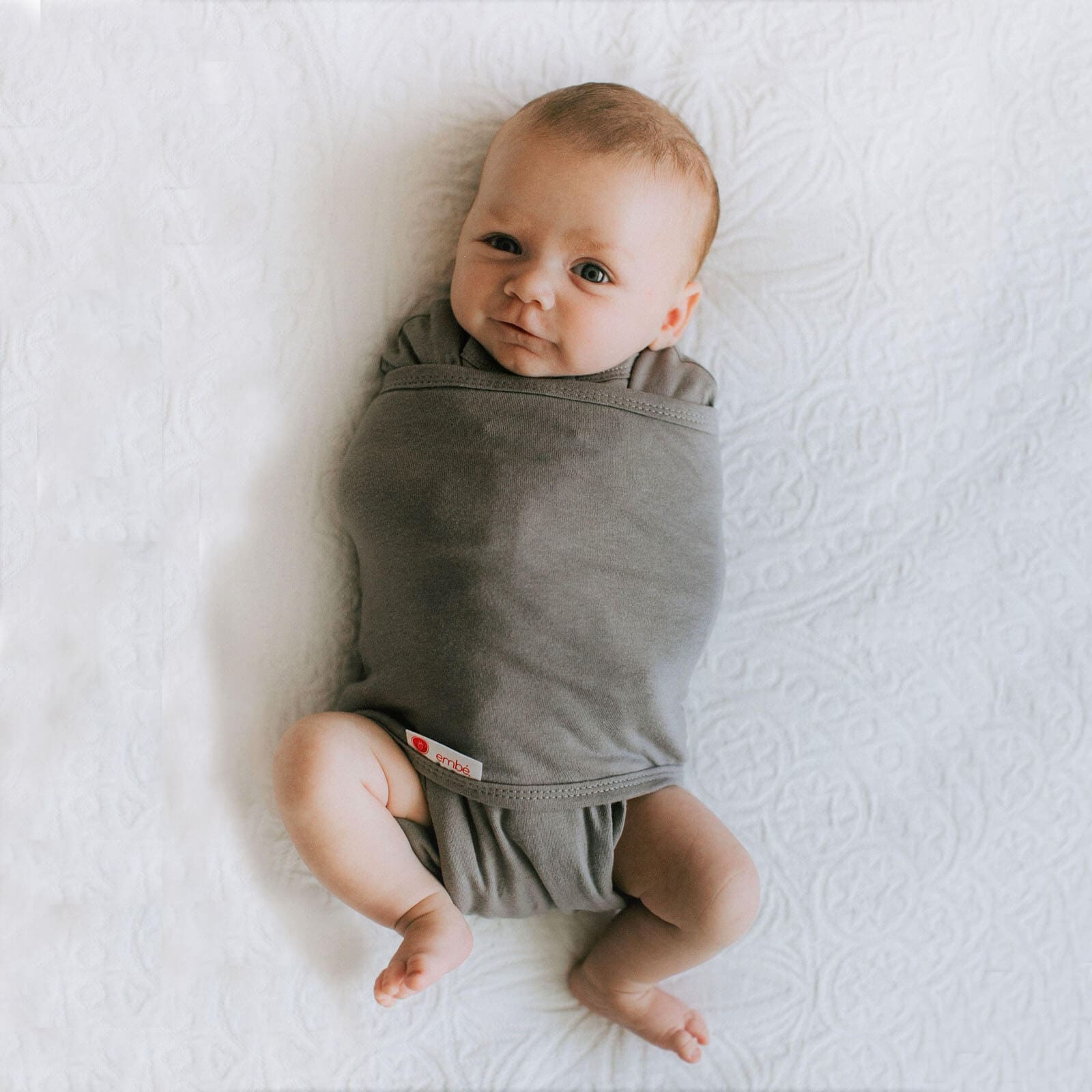 Baby wrapped in grey swaddle laying in a white background
