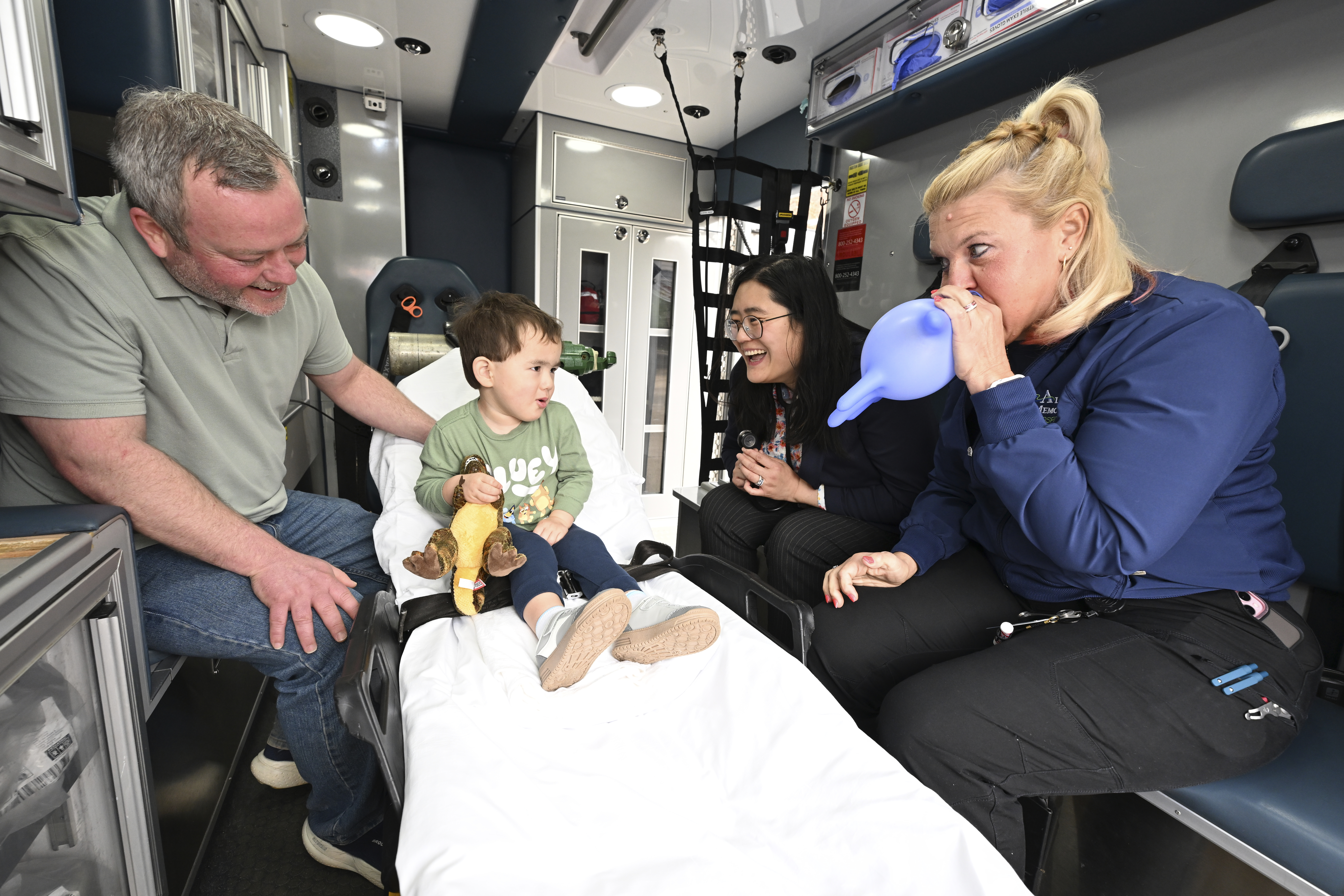 Ben (left), Yaheng, and paramedic (right most) interact playfully with the son in the ambulance bed