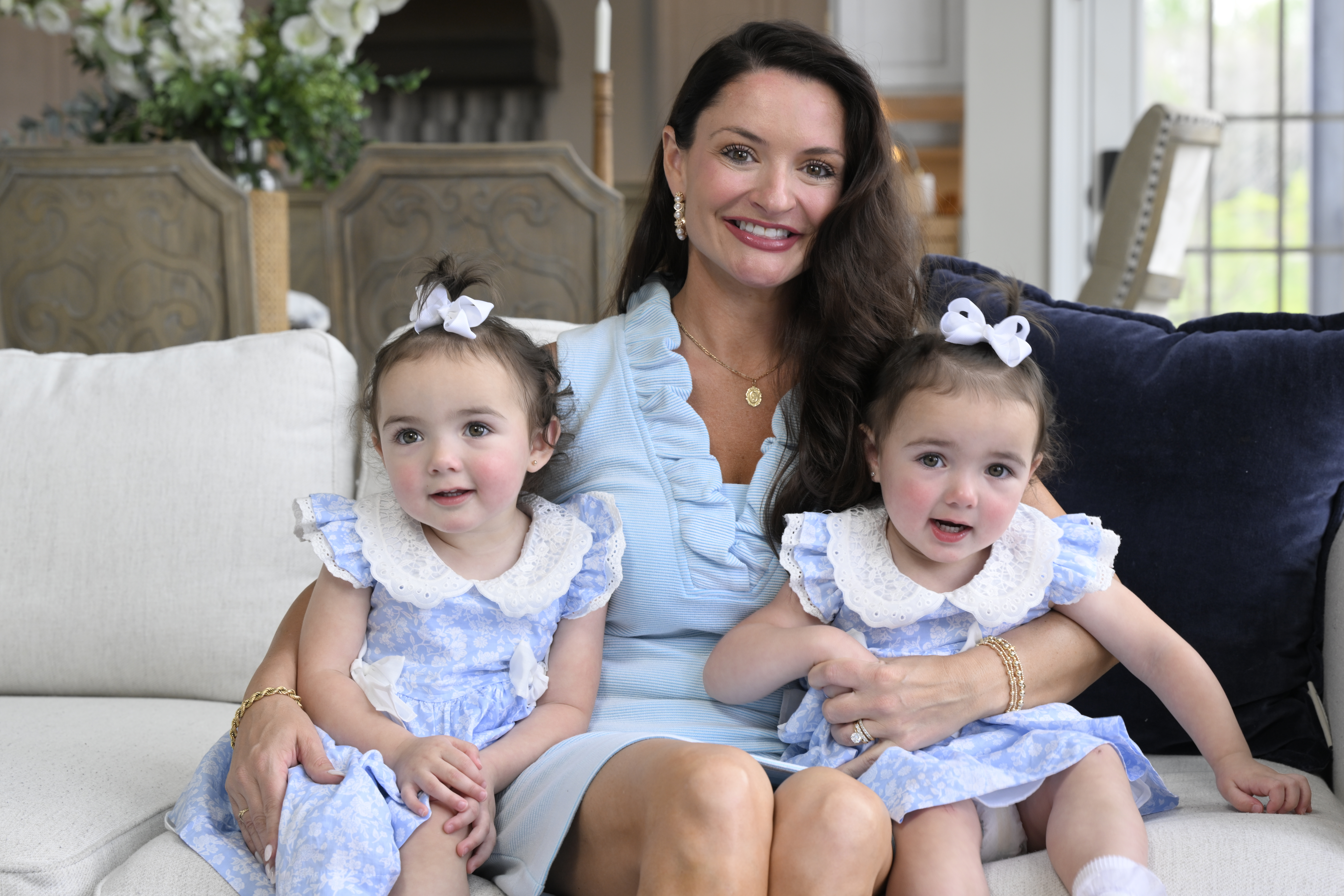Casey seated on cream couch, holding twin daughters, all in light blue dresses