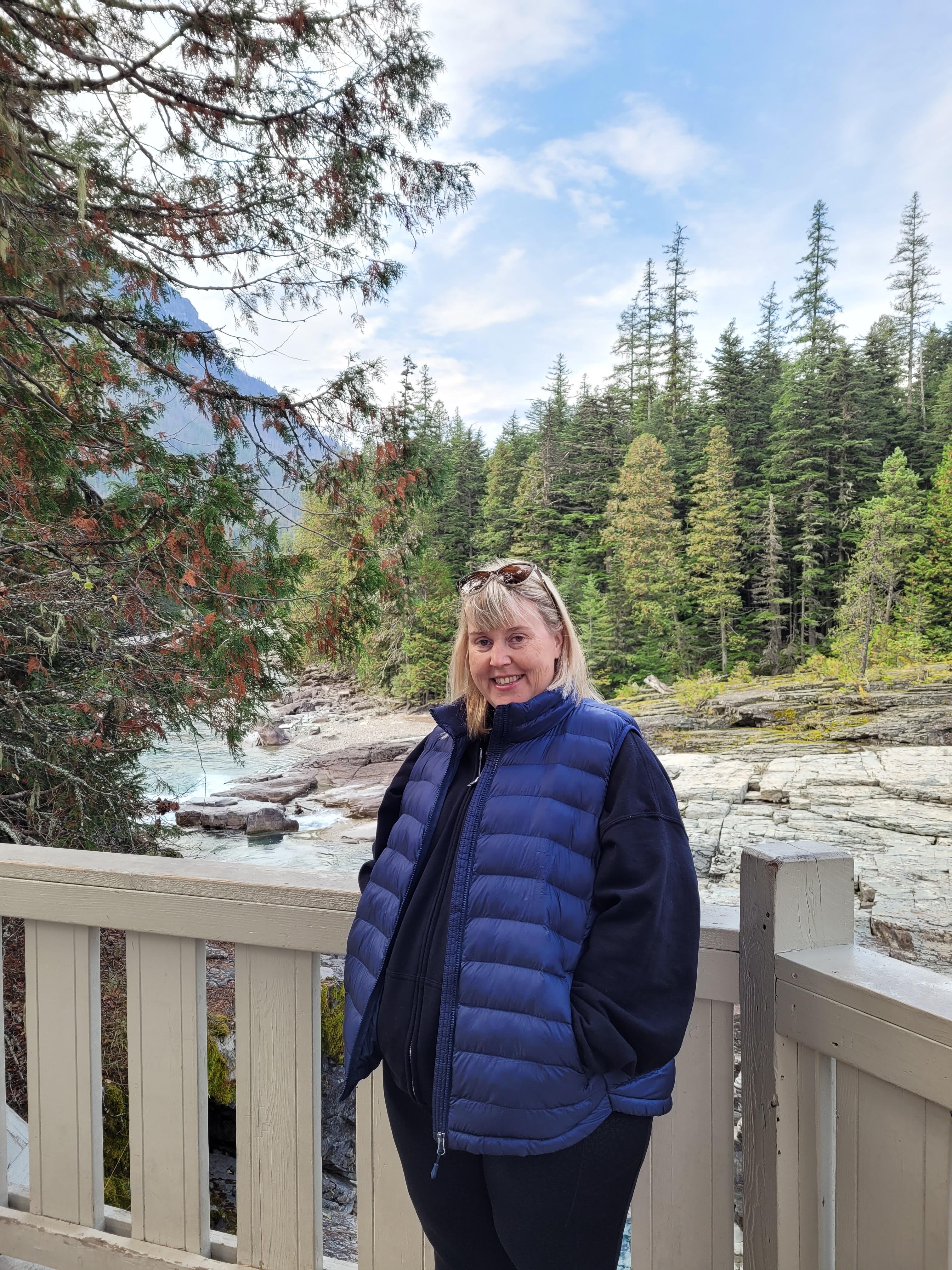 Patient Heather Taylor standing on a balcony with a river and pine forest in the background