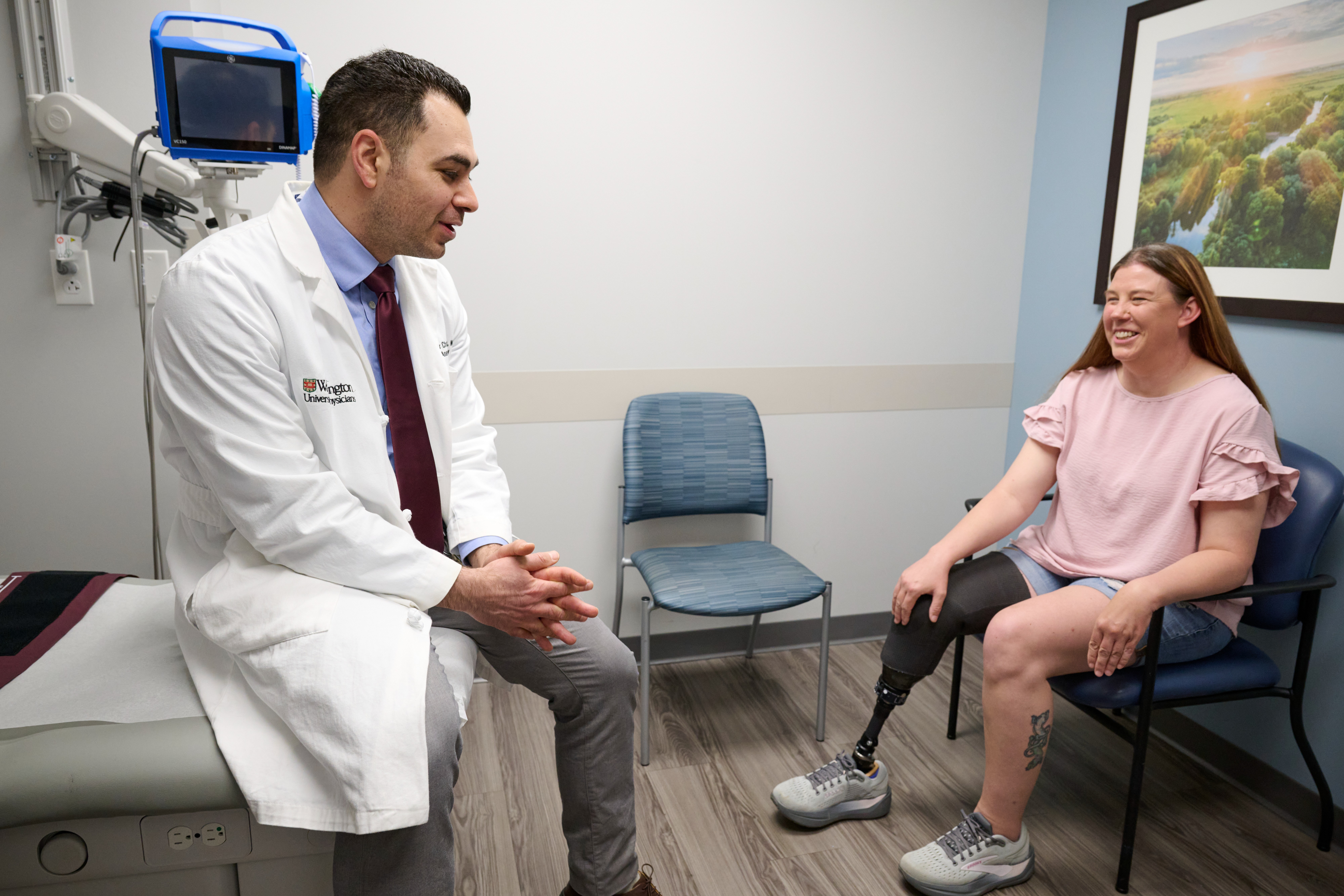 Dr Alexander Chamessian seated on clinic table, talking to patient Jodi Evans, seated on a chair nearby 