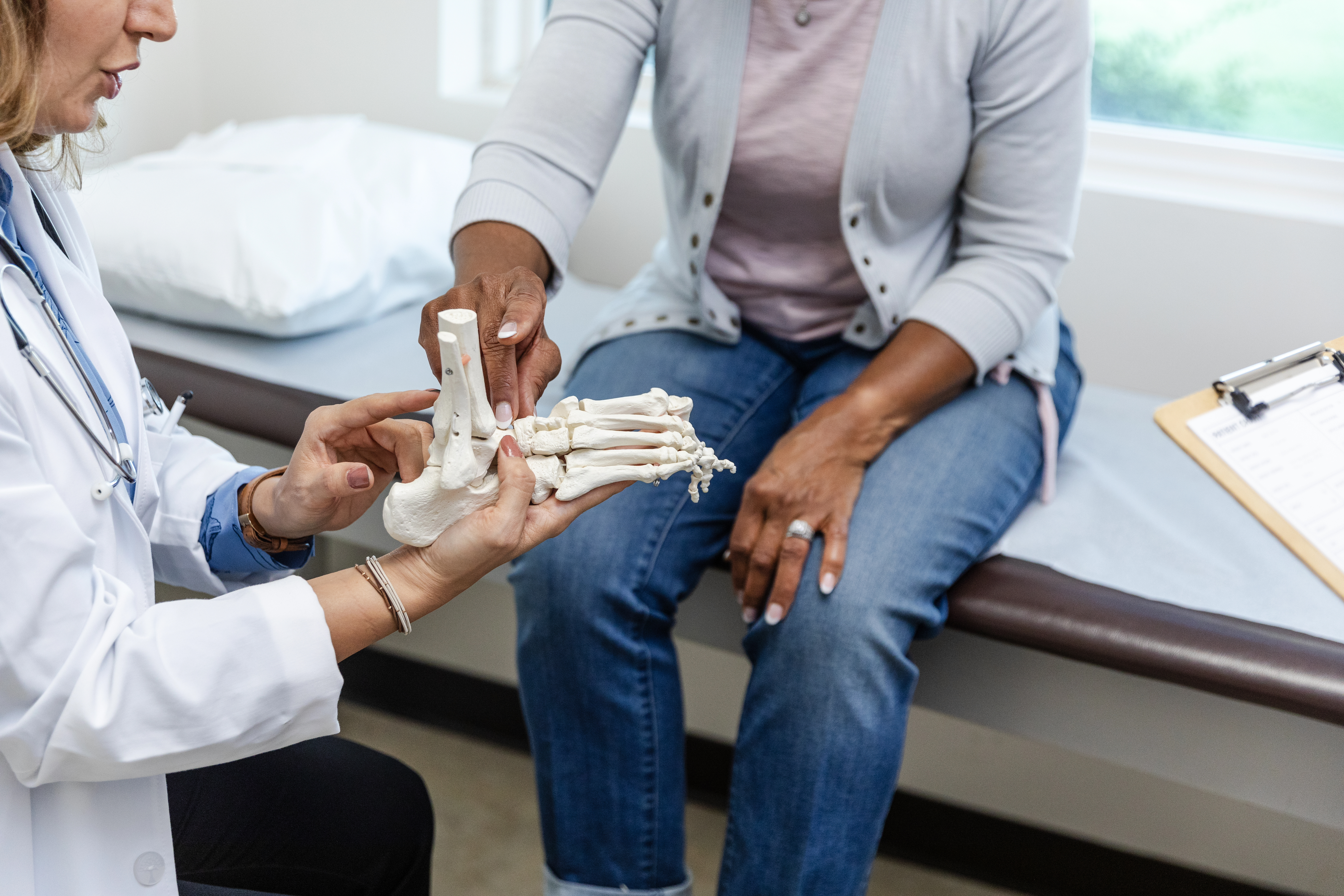 Doctor (left) shows foot skeleton clay model to a patient sitting down