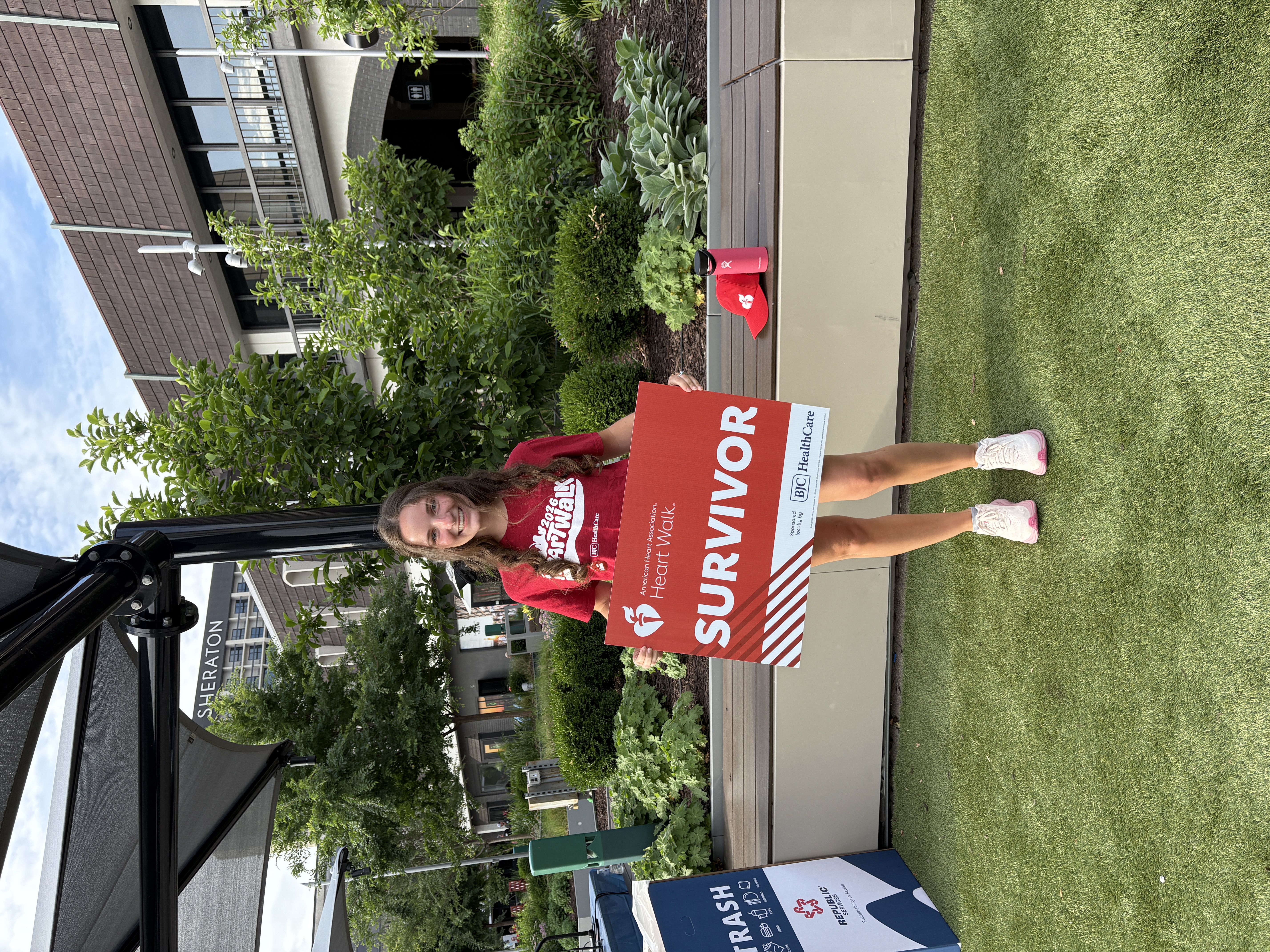 Abigail Ellis in a red shirt, holding a red American Heart Association Heart Walk sign that reads "SURVIVOR" int he middle