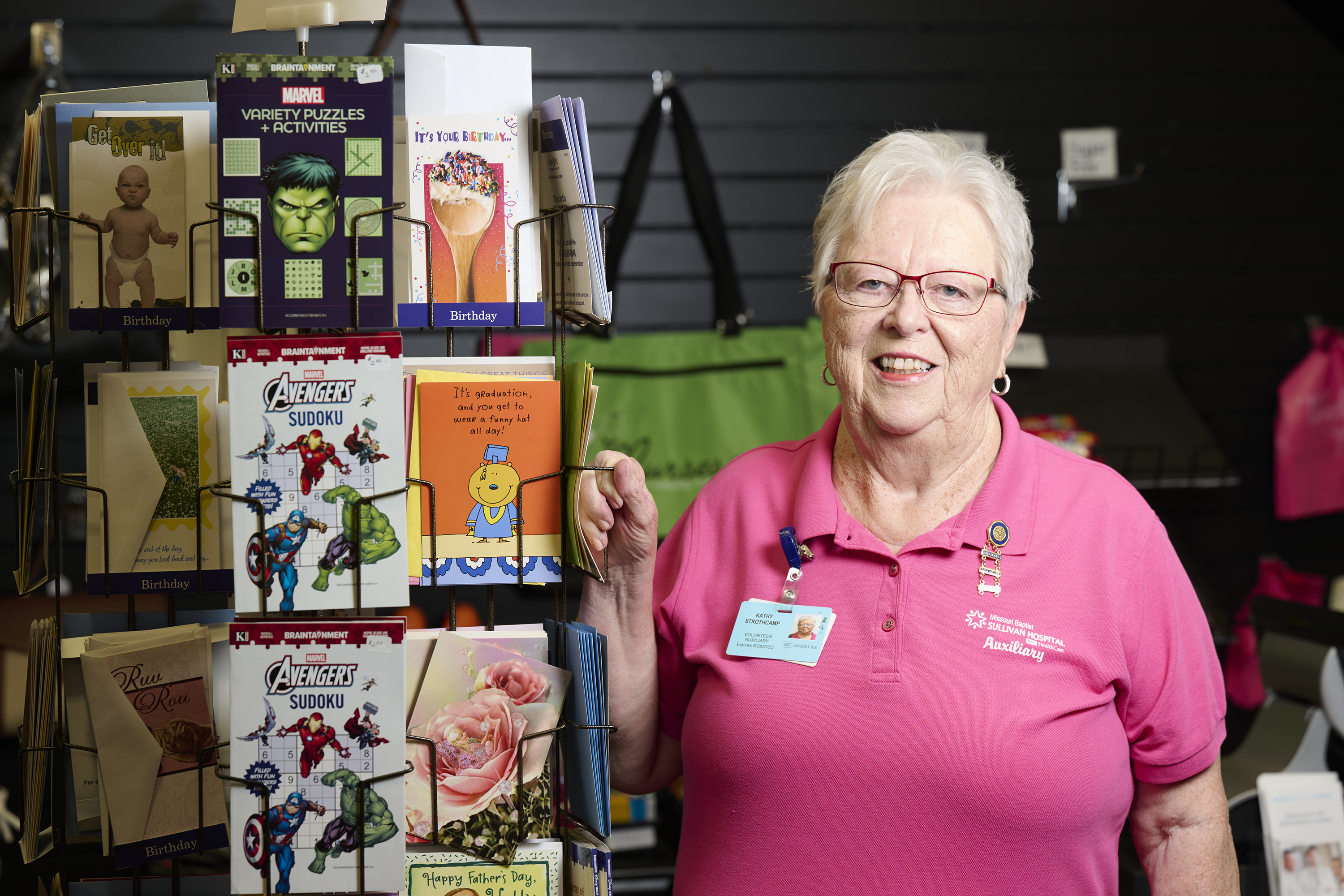 Kathy in a pink t-shirt, posing next to a rack of greeting cards