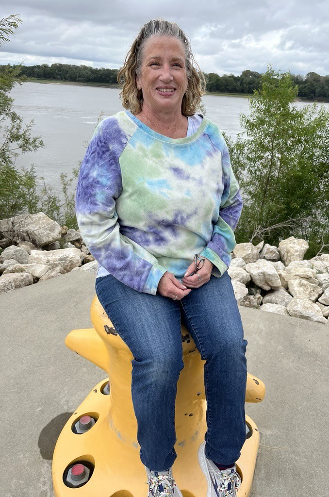 Patient LeAnn Areford sitting by a river smiling.