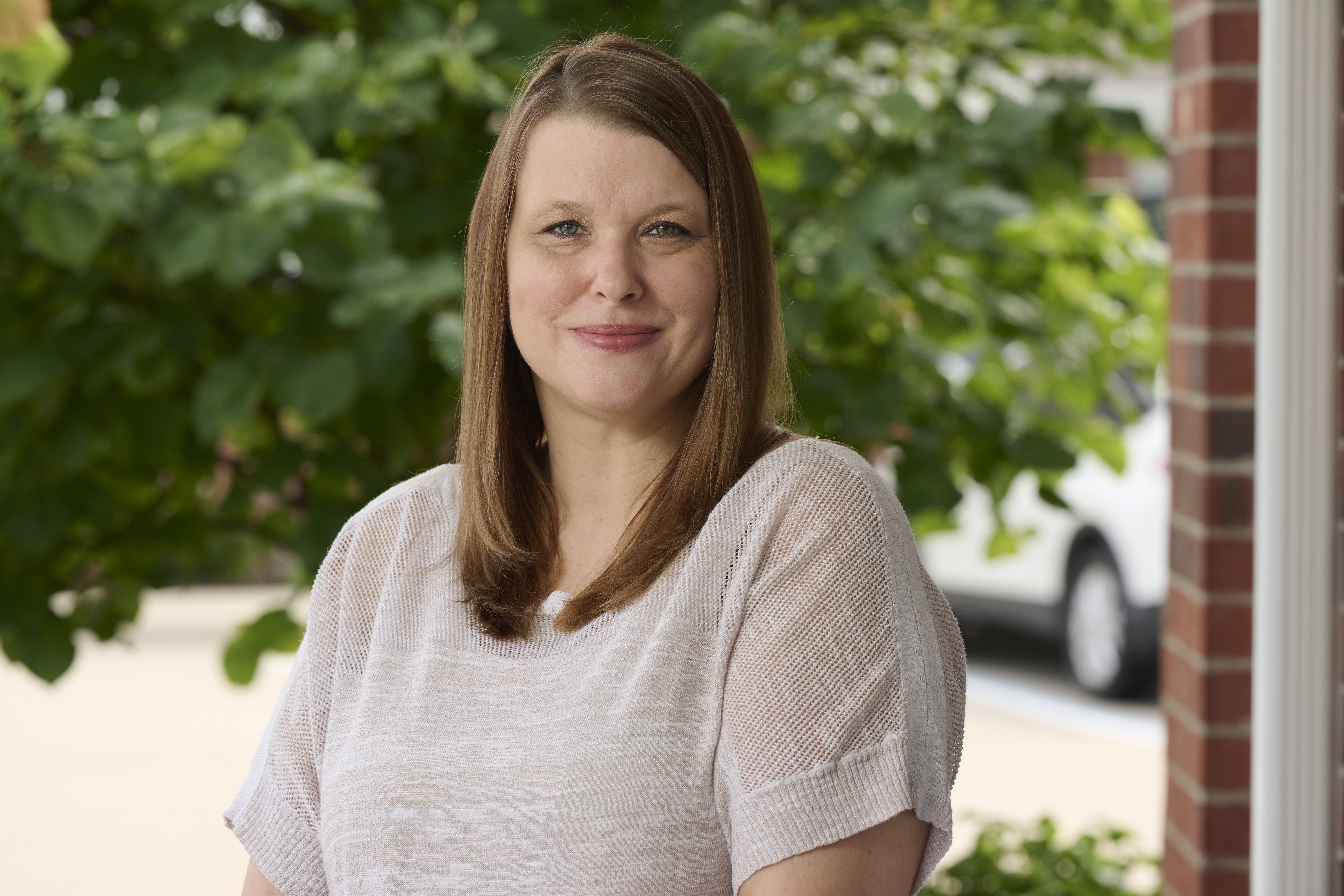 Headshot of stroke survivor Monica McCloud in a white t-shirt and outdoor background with tree branches and leaves