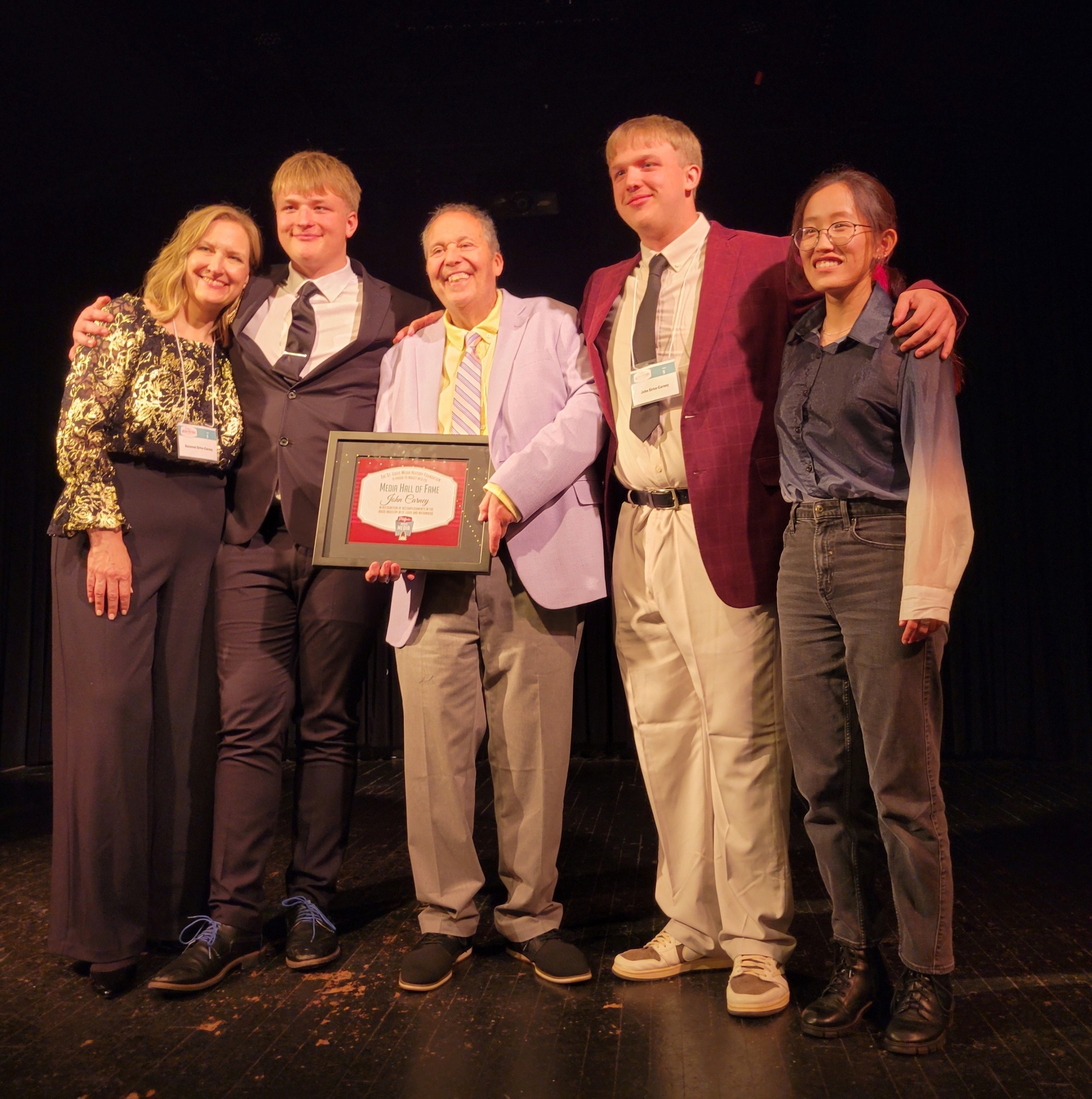 John Carney (center) poses on stage with an award next to his wife and three children 