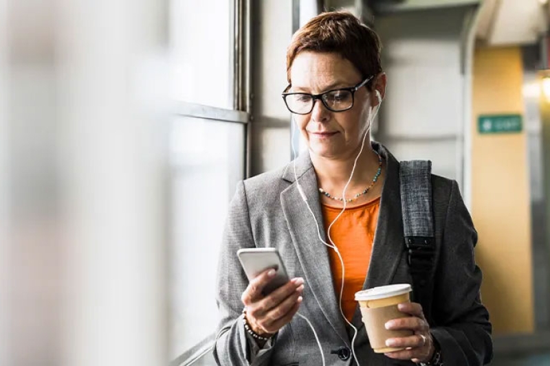 Woman with headphones looking at her phone and holding a cup of coffee