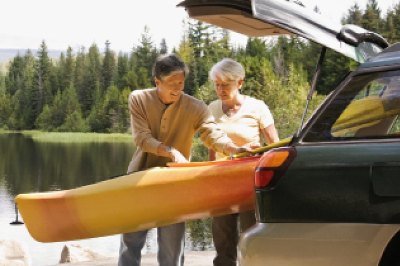 Woman and man standing outdoors next to a canoe and car