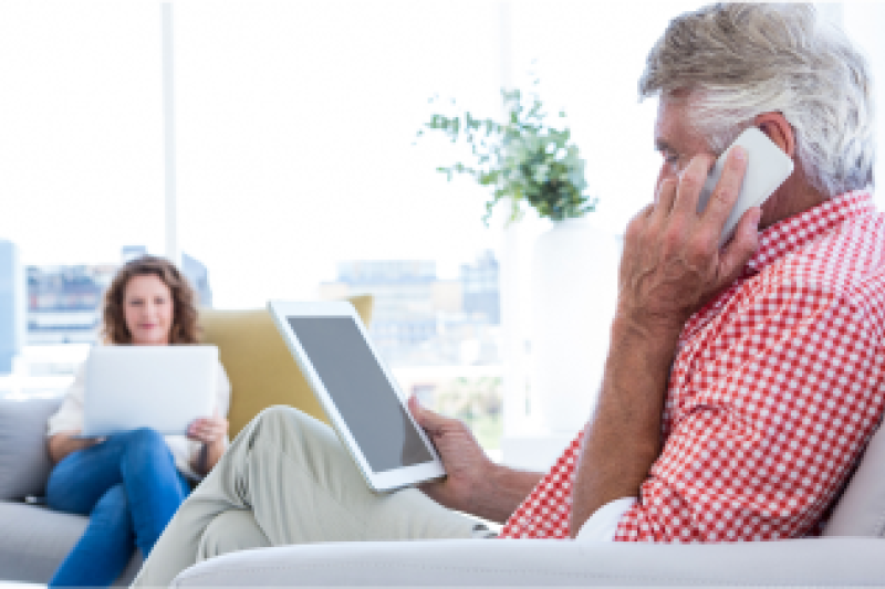 Woman and man sitting, with man talking on the phone and looking at a tablet and the woman using her laptop