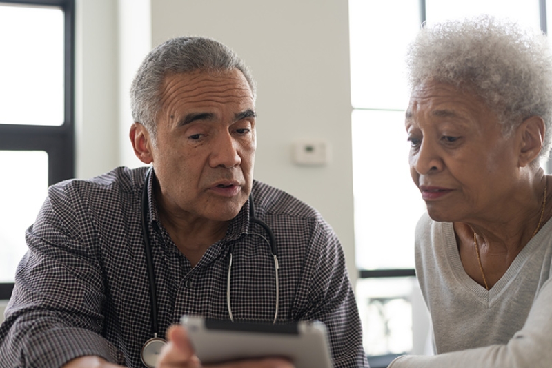 Two people sitting at a table talking and looking down at a tablet