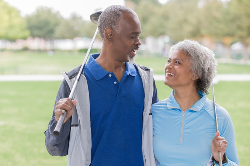 Couple holding golf clubs and smiling at eachother