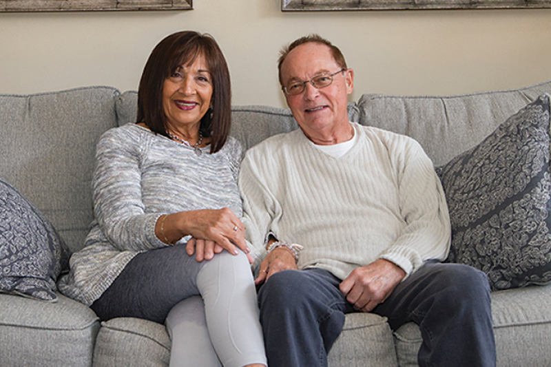 Robert Malon, 74, sitting with his wife on a couch.