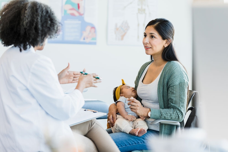 A woman holding a newborn baby and talking to a doctor