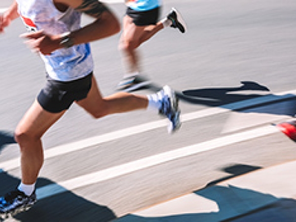 Stock image of three runners, pictured neck down in shorts,sleeveless shirts, and tennis shoes on a race track