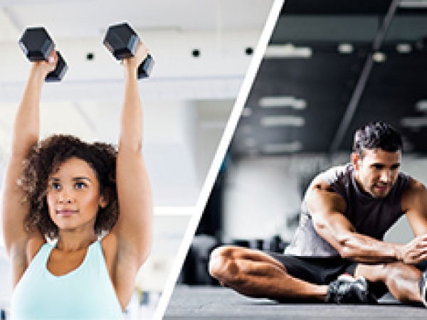 Stock image of half body shot of woman holding up two dumbbels and a seated male stretching one leg in front of him