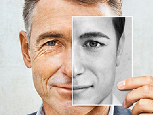 A man holding a black and white image of a half face against the left side of his own face